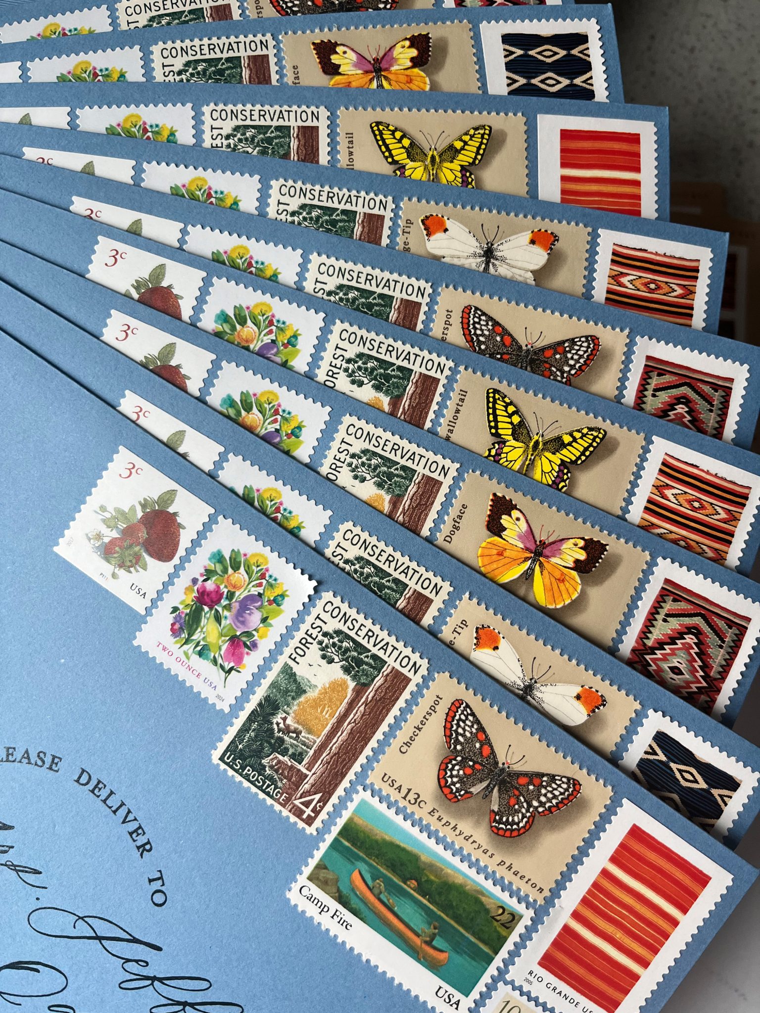 A collection of vintage postage stamps arranged on the corner of blue wedding guest envelopes.