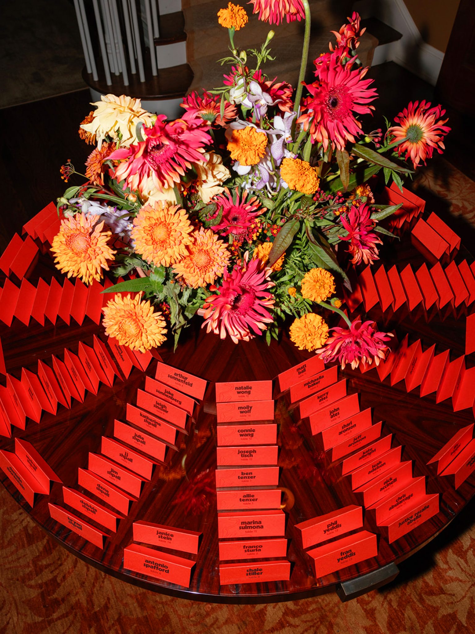 Folded orange escort cards on a round table with a floral display in the center